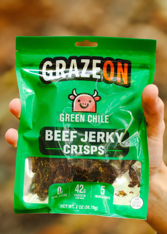 Green package of Graze On Green Chile Beef Jerky Crisps held in a hand with a blurred natural background