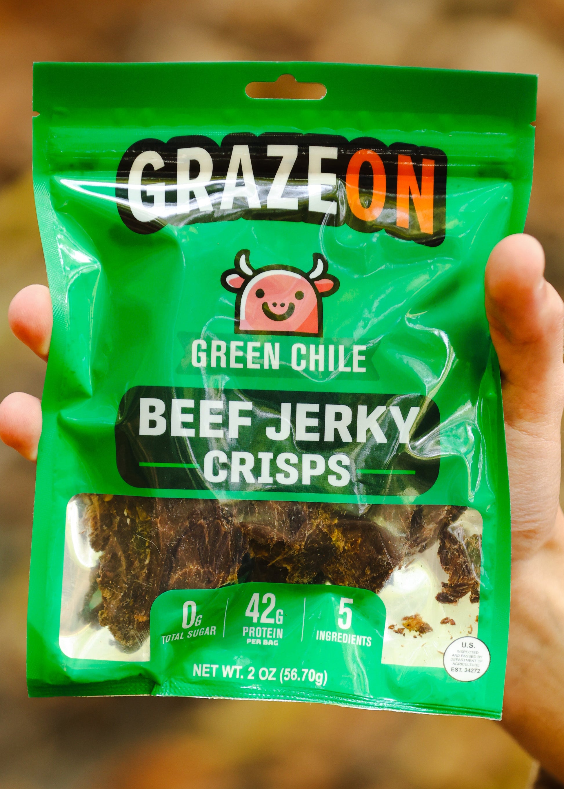 Green package of Graze On Green Chile Beef Jerky Crisps held in a hand with a blurred natural background